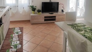 A modern living room with a flat-screen TV on a wooden stand, a dining area with a table and chairs, and a kitchen area with a sink and cabinets. - Palmi Bay Home (Palmi)