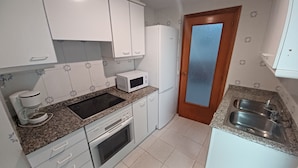 A compact kitchen with white cabinets, a microwave, a coffee maker, a stove, and a sink.