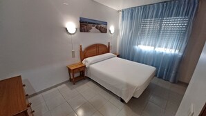 A bedroom with a wooden bed, a nightstand, a wall-mounted light, and a window with curtains.