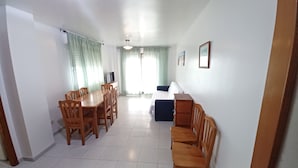 A spacious living area with a dining table and chairs, a sofa, and a TV on a stand.