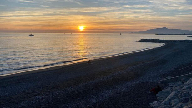 A beach with a calm sea, a sunset, and a distant mountain. - Appartamento Casa NUNI (Lavagna)