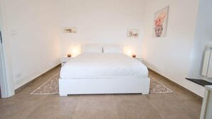A bedroom with a large bed, two bedside tables, and a nightstand. - Appartamento Casa NUNI (Lavagna)