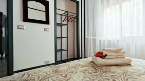 A hotel room with a bed, a mirror, a wardrobe, and a window with sheer curtains.