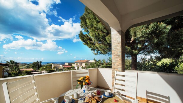 A balcony with a table set for breakfast, overlooking a coastal view.