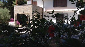A two-story house with a stone facade, wooden balcony, and a garden with flowering plants.