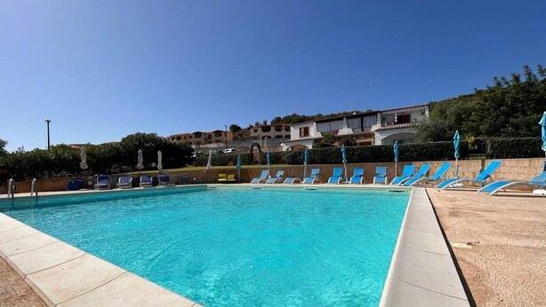Una piscina amb gandules i ombrelles blaves, envoltada per un solàrium de formigó.