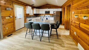 Une cuisine moderne avec des murs en bois, un îlot central doté de tabourets de bar, des appareils en acier inoxydable et un plancher en bois clair.