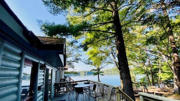 Une terrasse dotée d’un jacuzzi, d’un espace salon extérieur et offrant une vue sur un lac entouré d’arbres.