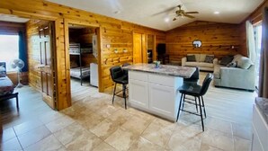 L’intérieur d’une cabane comprend un coin cuisine avec un aménagement en bois, une table à manger avec des chaises et un canapé dans l’espace salon.