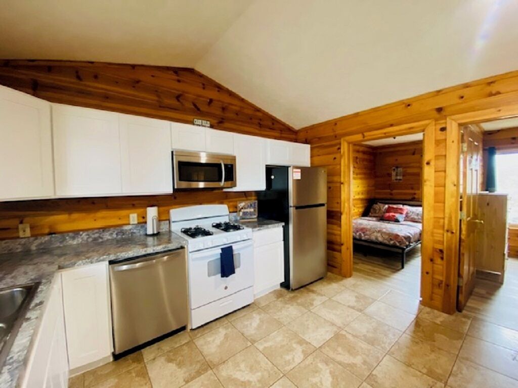 A compact kitchen with white cabinets, stainless steel appliances, and a wooden ceiling.