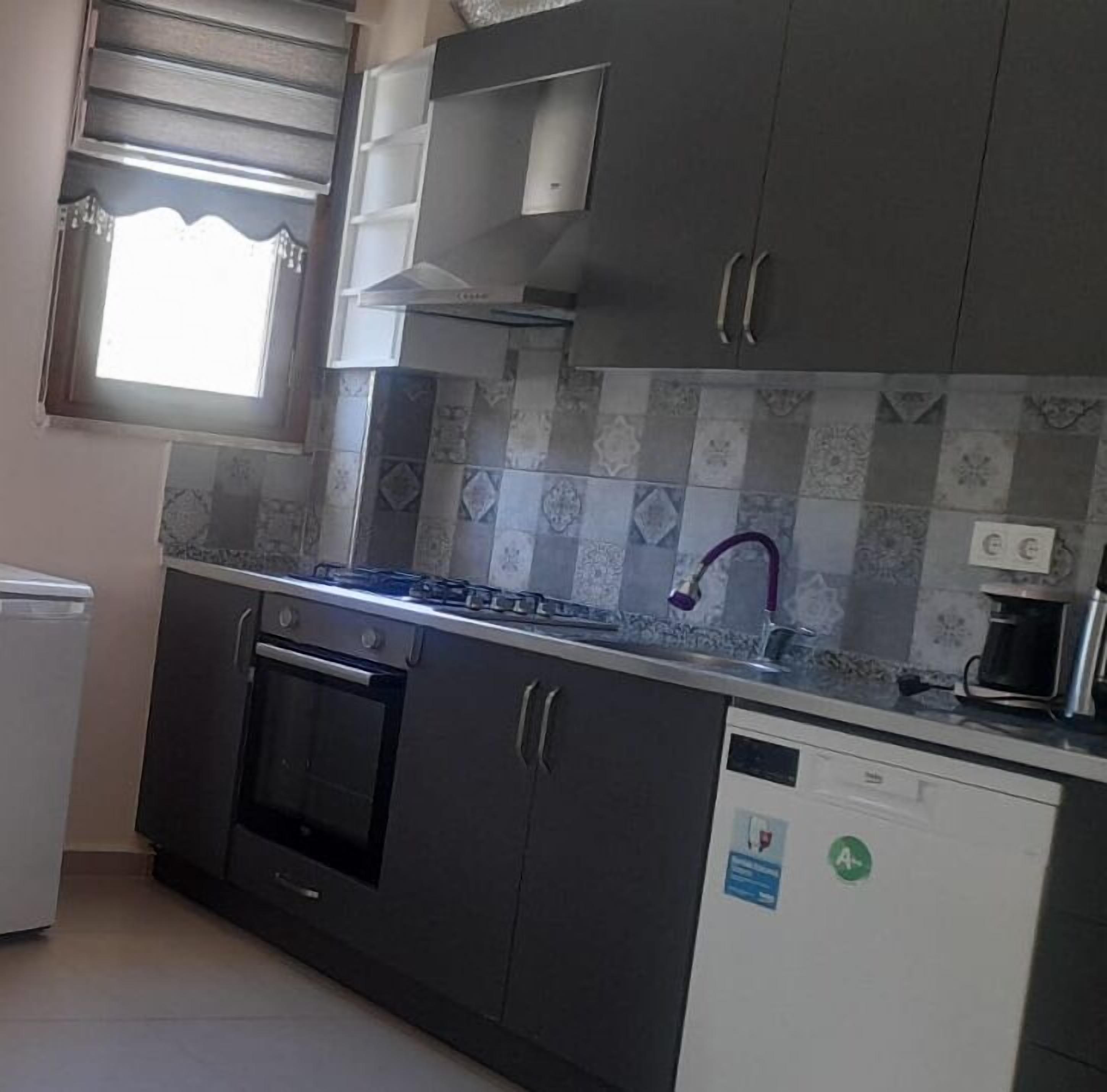 A kitchen with a gas stove, oven, and dishwasher. There is a window with blinds, a sink with a purple faucet, and a coffee maker on the counter.