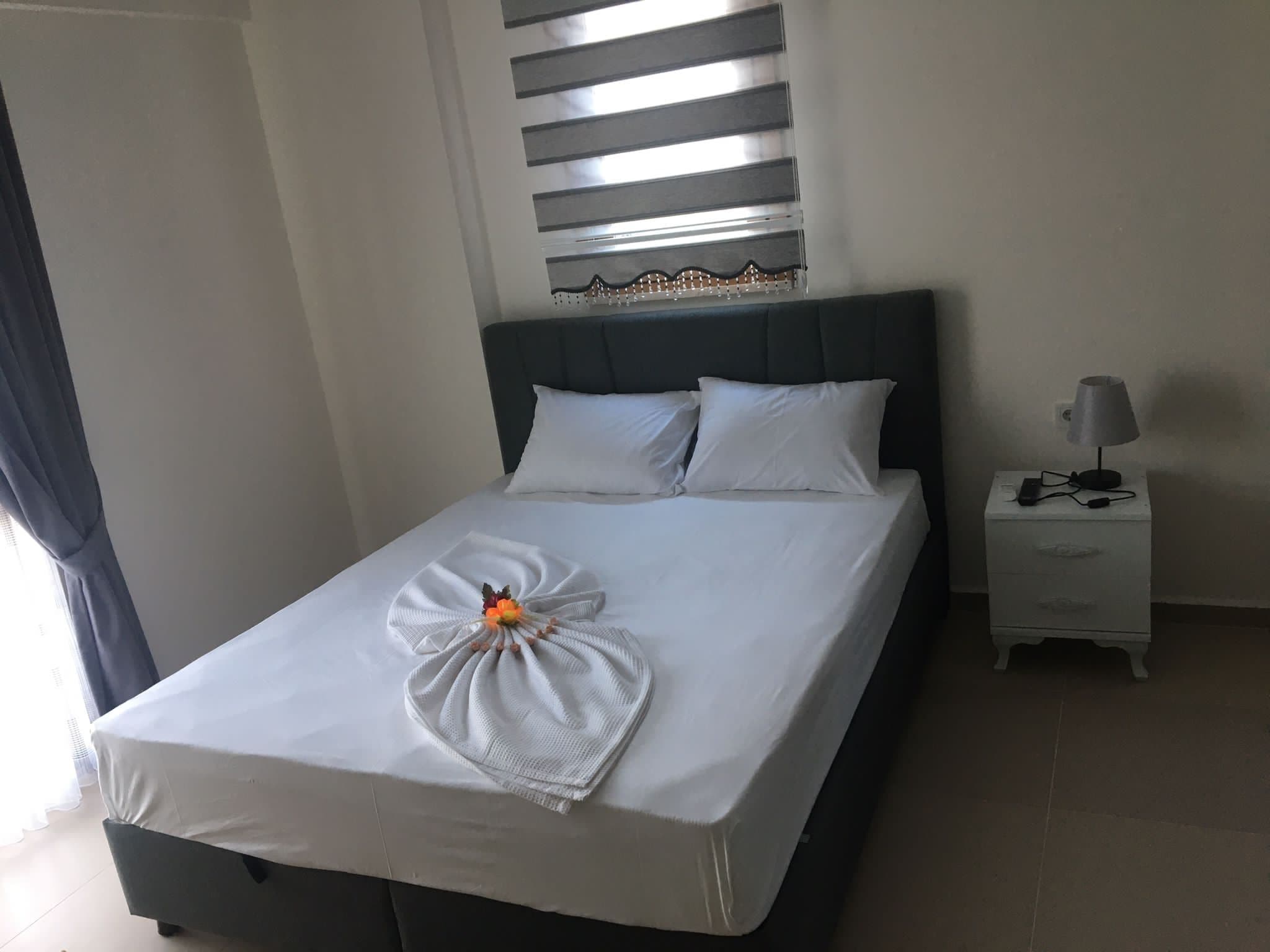 A neatly made bed with a towel and flower arrangement, a bedside lamp, and a nightstand with a lamp.