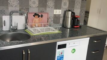 Una cucina compatta con lavastoviglie, macchina da caffè e scolapiatti.