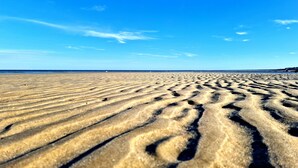 Een zandstrand met duidelijke voetafdrukken en een helderblauwe lucht.