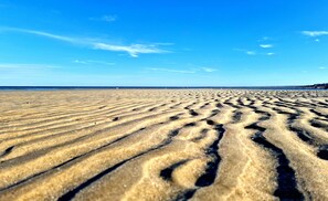 Una playa arenosa con huellas visibles y un cielo azul despejado.