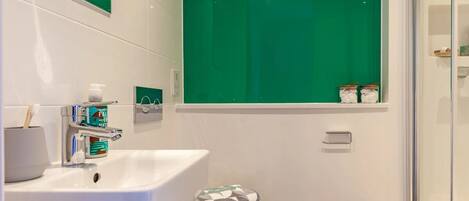 A modern bathroom with a white sink, green-tiled walls, and a toilet with a patterned towel.