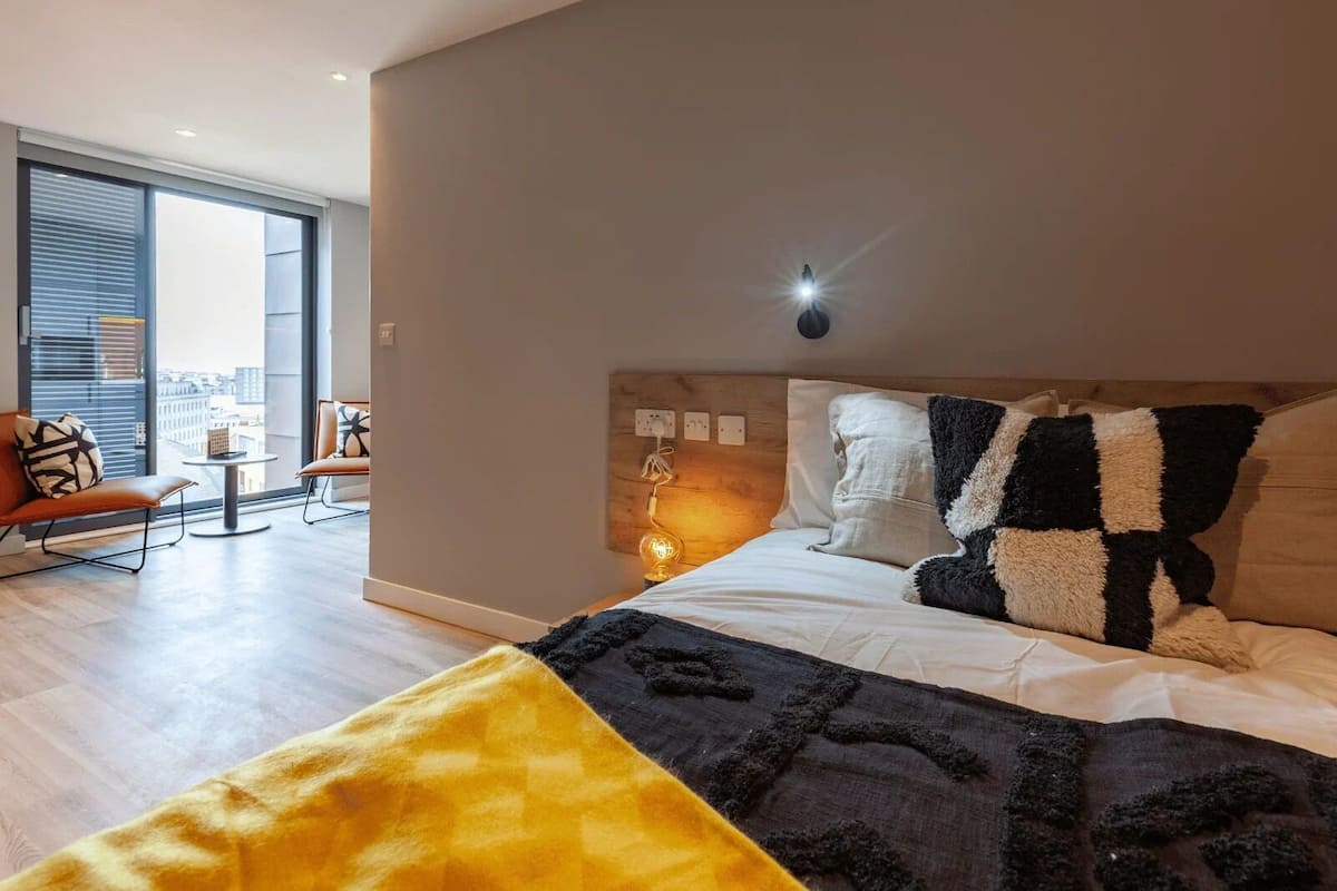 Une chambre d’hôtel moderne avec un grand lit, une petite table et une vue sur la ville grâce à de grandes fenêtres.