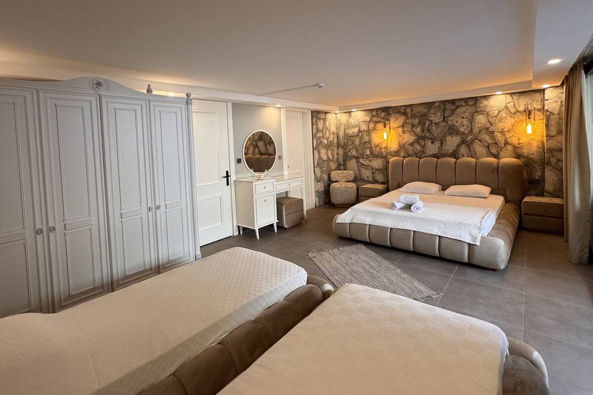 A bedroom with two beds, a vanity with a mirror, a stone accent wall, and a large wardrobe.