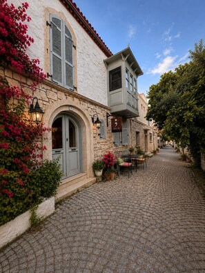 A cobblestone street with a building featuring a stone facade, a balcony, and outdoor seating. - No9 Alacati (Cesme)