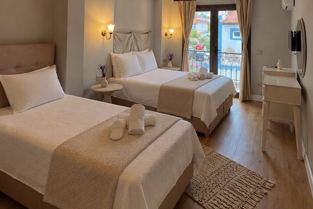 A hotel room with two beds, a balcony, a small table, and a ceiling with exposed beams.