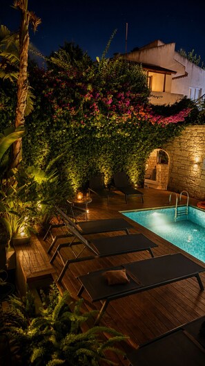 A poolside area with lounge chairs, a stone wall, and a building in the background. - No9 Alacati (Cesme)