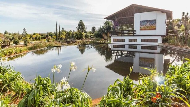 A modern building with a glass facade reflecting a pond and surrounding greenery. - Quarto Privativo com Suite e Ar (São Sebastião)