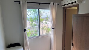 A room with a window, a chair, an air conditioner, and a wooden door. - Quarto Privativo com Suite e Ar (São Sebastião)