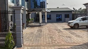 Una strada asfaltata conduce a un edificio dal design moderno, con un SUV bianco parcheggiato nelle vicinanze e una piccola costruzione con colonne di fronte.