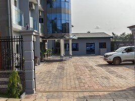 Un camino pavimentado que conduce a un edificio de diseño moderno, un SUV blanco estacionado cerca y una pequeña construcción con columnas al frente.