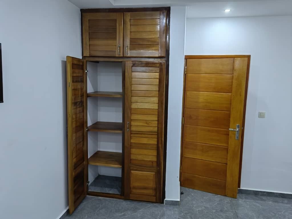 Habitación en esquina con un armario de madera, una puerta y suelo de baldosas.
