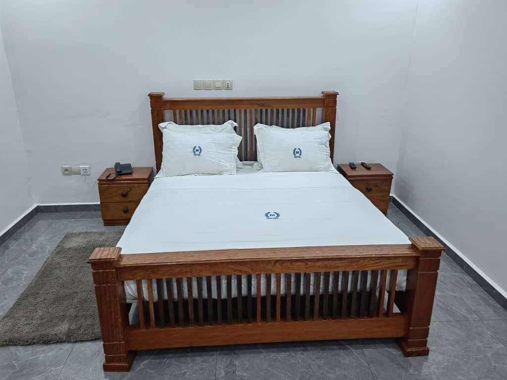 Un dormitorio con cama de madera, dos mesitas de noche y un enchufe en la pared.