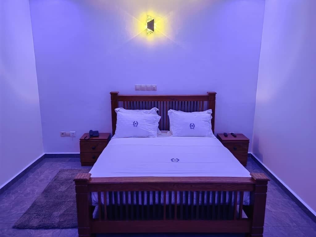 Une chambre à coucher avec un lit en bois, deux tables de chevet, une petite table et un luminaire fixé au mur.