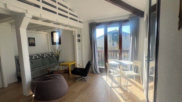 Een moderne woonkamer met een hoogslaper, een bank, een salontafel en een eethoek met stoelen.