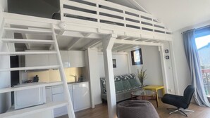Een moderne loft slaapkamer met een stapelbed, een keukenhoek en een zithoek met een ronde tafel en stoelen.