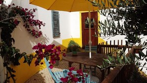 Une terrasse avec une table et des chaises en bois, entourée de plantes et de fleurs en pot.