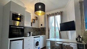 A modern kitchen with built-in appliances, a dining area with bar stools, and a large window providing natural light. - APPARTEMENT PARIS CDG COSY ET LUMINEUX (Livry-Gargan)