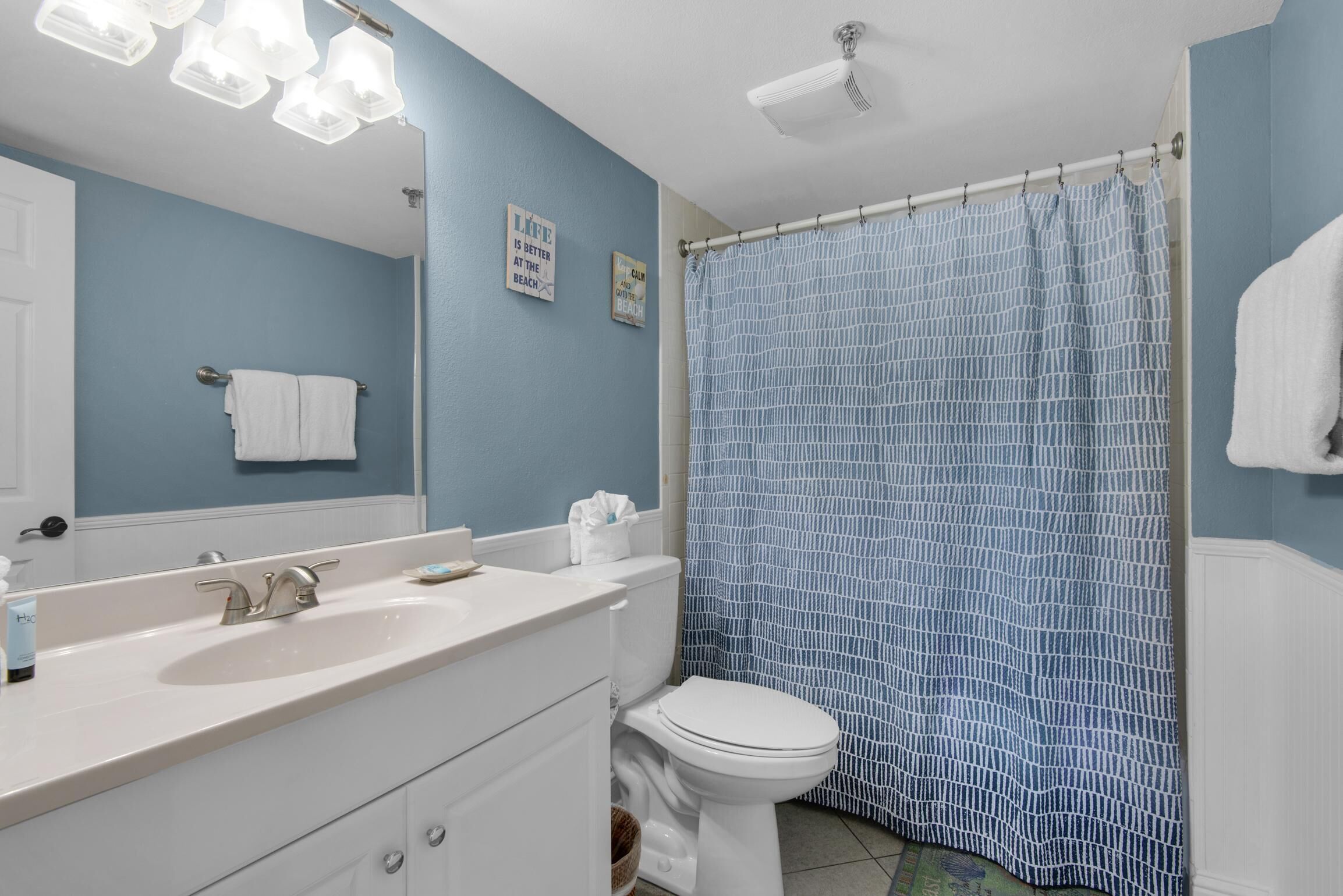 A bathroom with a white sink, a toilet, a blue shower curtain, and a towel rack.