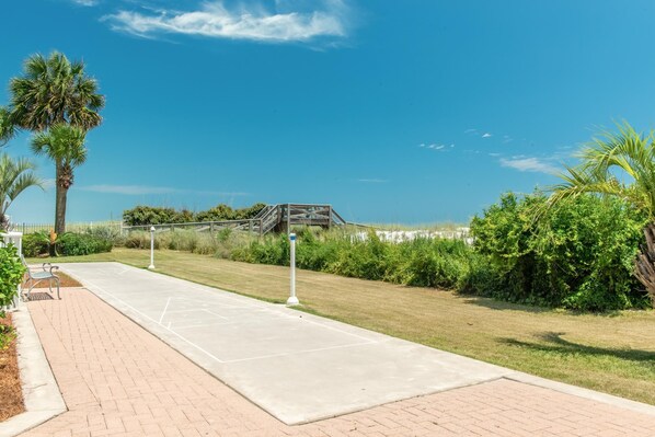 A paved pathway with benches, palm trees, and a wooden structure in the distance. - Destin on the Gulf 303 (Destin)