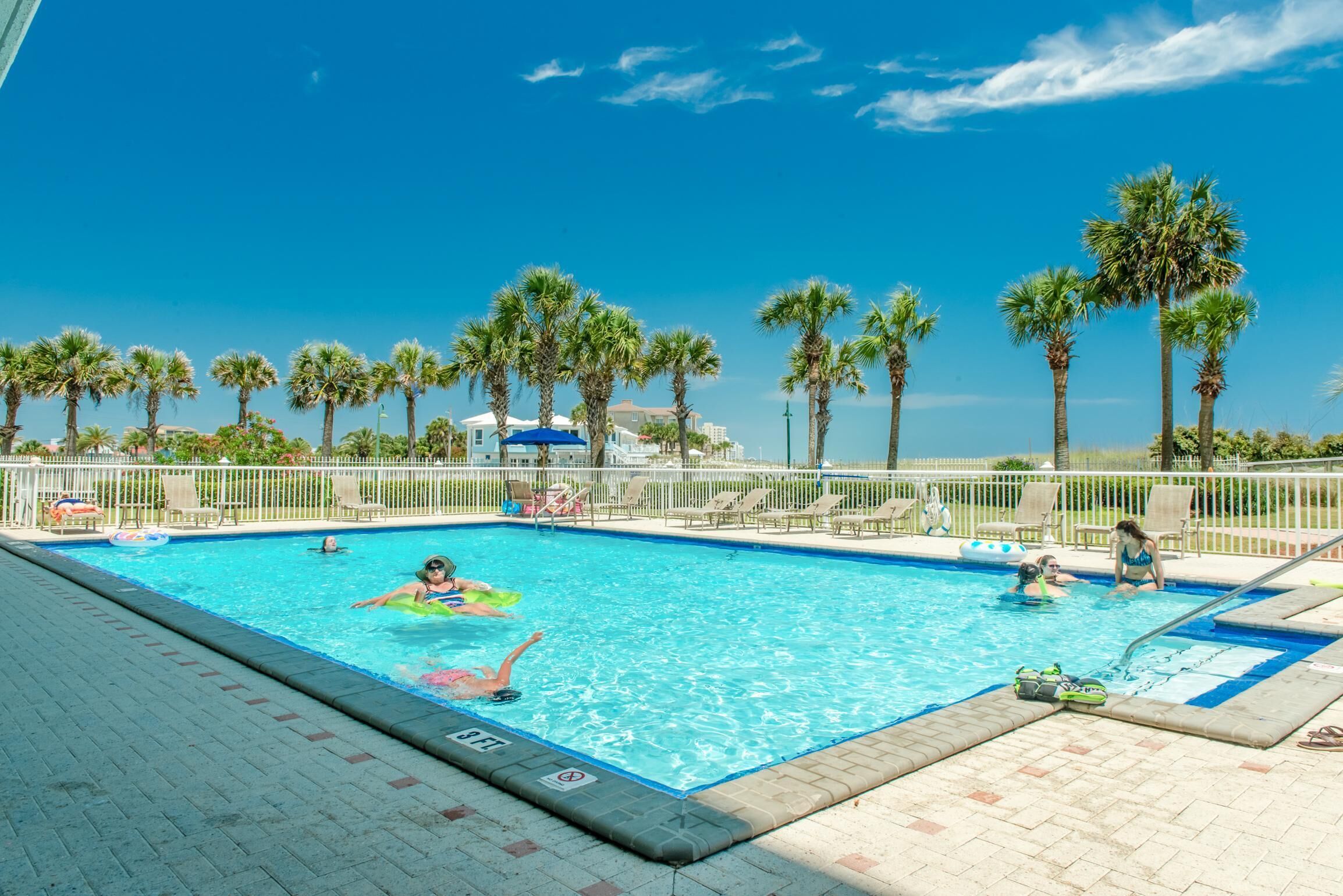 A swimming pool with palm trees, lounge chairs, and a clear blue sky.