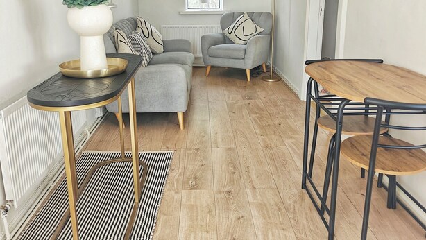 A modern living room with a grey sofa, a round coffee table, and a dining table with chairs. There is a potted plant on the coffee table and a floor lamp beside the sofa. - The Curragh Studio (Cut Bush)