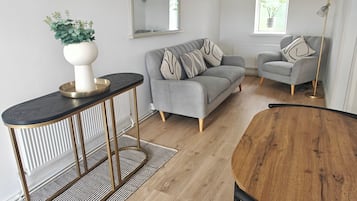 A modern living room with a grey sofa, a round wooden dining table, and a black and white patterned rug.