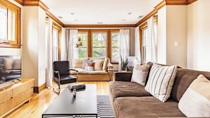 A spacious living room with a large flat-screen TV, a brown sofa, a black chair, and a wooden coffee table. - 15min Drive to Med District.20min Dr to Fulton Mkt. Direct Bus to Union Station. (Chicago)