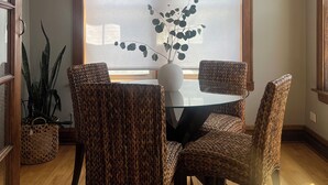 A dining area with a round glass table, four woven chairs, a vase with green foliage, and a large window with blinds. - 15min Drive to Med District.20min Dr to Fulton Mkt. Direct Bus to Union Station. (Chicago)