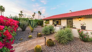 Una casa con tetto in tegole rosse, un vialetto in pietra e diversi cactus e fiori.