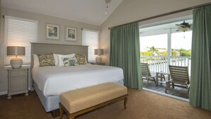 Een slaapkamer met een groot bed, twee bedlampen, een plafondventilator en uitzicht op een balkon met buitenmeubilair.
