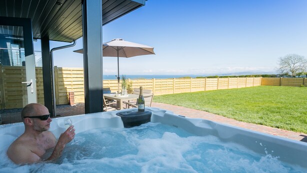 A man in a hot tub with a view of the ocean. - 2 Trem Y Mor -  a dog that sleeps 6 guests  in 3 bedrooms (Moelfre)