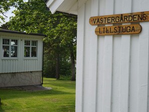 A wooden sign with the text "Västergårdens Lilstuga" mounted on a white wall.