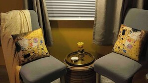 A cozy seating area with two armchairs, a small round table with a flower vase, and a window with blinds. - Gustav Klimt The Kiss -Camper/RV in Saint Matthews, South Carolina (Saint Matthews)