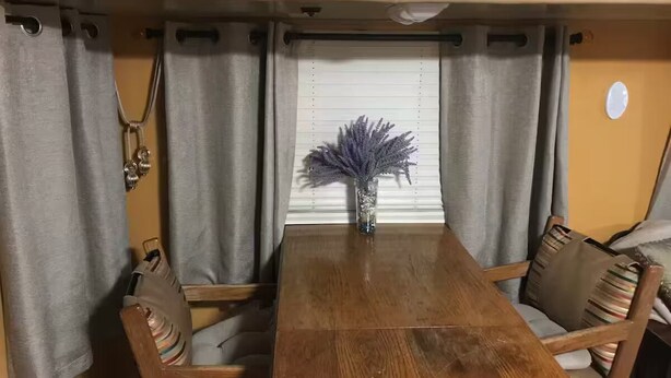 A dining area with a wooden table and chairs, a vase with flowers, and curtains. - Gustav Klimt The Kiss -Camper/RV in Saint Matthews, South Carolina (Saint Matthews)
