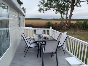 Un patio esterno coperto con tavolo e sedie, una ringhiera bianca e vista su un campo.